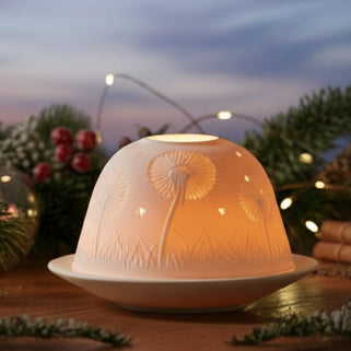 Decorative setup with a lamp, greenery, and small gifts on a wooden table against a blurred festive background.