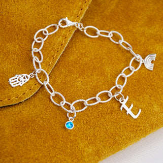 Personalised Sterling Silver Charm Bracelet with Blue Topaz/December birthstone, script Initial E charm, hamsa hand chime & rainbow chime. Shown in close up shot.