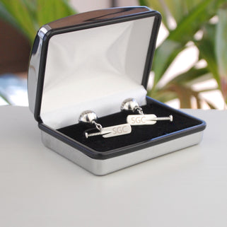 Cricket bat and ball cufflinks with personalised "SGC" initials engraved on both bats, shown in silver chrome rectangle cufflinks box.