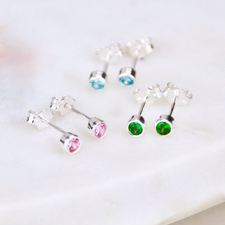 close up shot of silver birthstone stud earrings in Aquamarine/March, June/Alexandrite & May/Emerald.