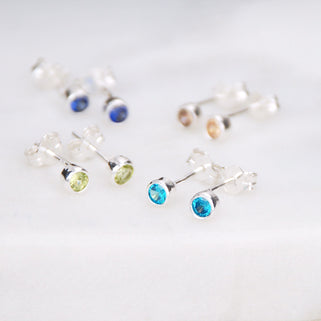 close up shot of silver birthstone stud earrings in August/Peridot, November/Citrine, December/Blue Topaz & September/Sapphire.