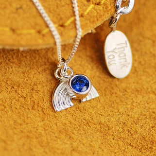 Necklace with silver rainbow charm and September/Sapphire birthstone with personalised engraved "Thank You" silver oval disc on the back of necklace shown in close up shot