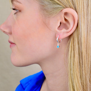 Sterling Silver Huggie Hoop Earrings with Blue Topaz/December birthstone charm, shown close up on model