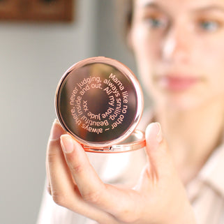 Rose gold compact mirror with personalised spiral message engraved on the front, shown in close up shot held by model.