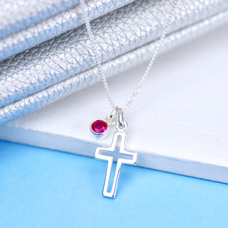 Silver cross charm necklace with July/Ruby birthstone charm, shown in close up shot