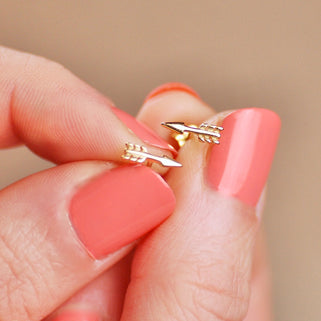 Pair of Tiny Gold Vermeil Arrow Stud Earrings shown in close up shot of model holding them