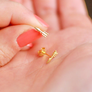 Pair of Tiny Gold Vermeil Arrow Stud Earrings shown in close up shot of model holding them