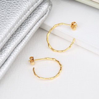 gold bevelled twist hoop earrings shown in close up shot on white background