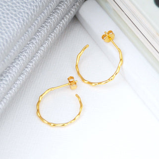 gold bevelled twist hoop earrings shown in close up shot on white background
