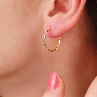 gold bevelled twist hoop earrings shown on model in close up shot