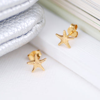 Mini gold starfish stud earrings shown in close up shot on white background