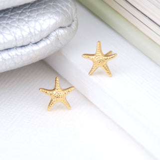 Mini gold starfish stud earrings shown in close up shot on white background