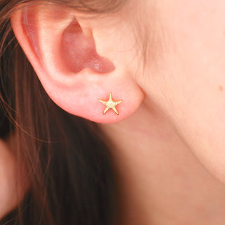 Mini gold starfish stud earrings shown in close up shot on model