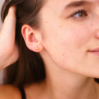 Mini gold starfish stud earrings shown in close up shot on model