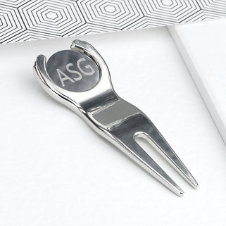 Golf divet repair and ball marker tool with "ASG" initials engraved on the front, shown in close up shot.