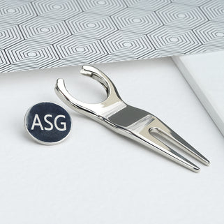 Golf divet repair and ball marker tool with "ASG" initials engraved, shown in close up shot.