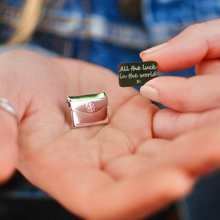 Lucky envelope pin and secret message letter with "All the luck in the world x" engraved on the front, shown in close up shot with model.