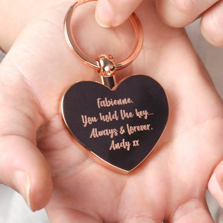 Rose gold heart keyring with personalised message "Fabienne you hold the key... Always & forever Andy xx" engraved on the front shown in close up with model.