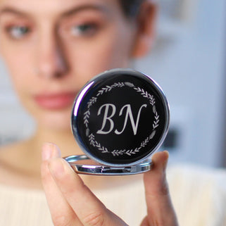 Silver compact mirror with personalised "BN" initials engraved in the centre with a floral wreath border, shown in close up shot with model
