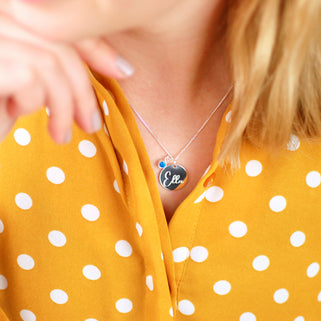 Necklace with personalised name "Ella" engraved on silver circle disc with Blue Topaz/December birthstone shown on close up shot on model