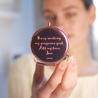 Rose gold compact mirror with personalised message "Keep smiling my gorgeous girl All my love Jem xxxx" engraved with heart icon beneath, shown in close up shot with model