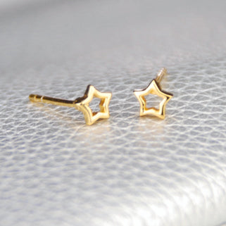 Gold vermeil tiny open star stud earrings shown in close up shot on grey background.