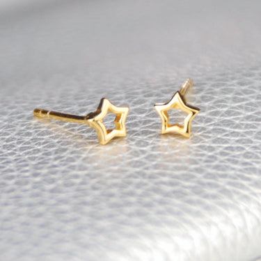 Gold vermeil tiny open star stud earrings shown in close up shot on grey background.