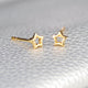 Gold vermeil tiny open star stud earrings shown in close up shot on grey background.