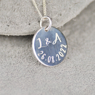 Sterling Silver Celebration Necklace. Silver round disc with "L&A 26.08.2022" engraved, shown in close up shot.