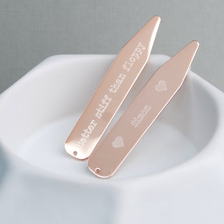 Rose gold collar stiffeners with "heart Simon heart" engraved on one and "Better stiff than floppy" engraved on the other, shown in close up shot.