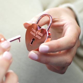 Rose gold lovers padlock and key with "Tom & Beth Paris 2020" engraved on the front, shown in close up shot with model.