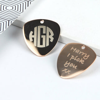 Gold guitar plectrums with personalised initials "HGR" engraved on one and "Harry I pick you xx" engraved on the other, shown in close up shot.