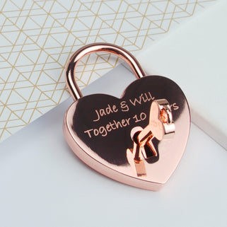 Rose gold lovers padlock and key with "Jade & Will Together 10 years" engraved on the front, shown in close up shot with key in padlock hole.
