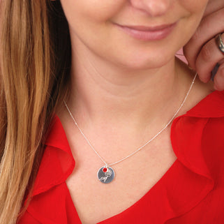 silver circle disc necklace with rose flower engraving and Ruby/July birthstone on satellite chain shown on close up of model