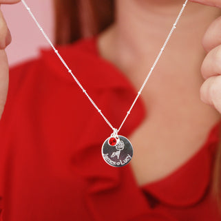 silver circle disc necklace with rose flower and "James heart Lucy" engraving and Ruby/July birthstone on satellite chain shown on close up of model