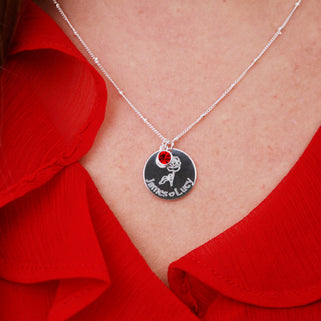 silver circle disc necklace with rose flower and "James heart Lucy" engraving and Ruby/July birthstone on satellite chain shown on close up of model