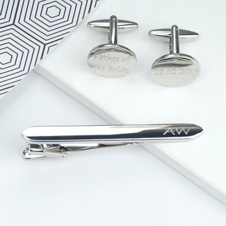Rounded silver tie clip and oval cufflinks set with personalised text, shown in close up shot.