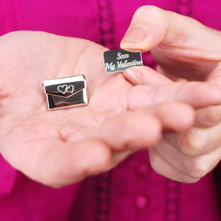 Love letter secret message pin with a double interlocking heart icon engraved on the front of the envelope and "Sam My Valentine" engraved on the letter, shown in close up with model.