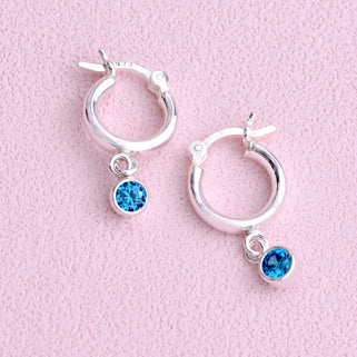 Sterling Silver Huggie Hoop Earrings with Blue Topaz/December birthstone charm, shown in close up shot