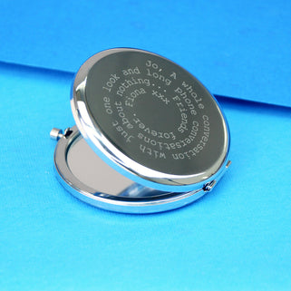 Silver compact mirror with personalised spiral message in typewriter font engraved on the front, shown in close up shot on blue background.