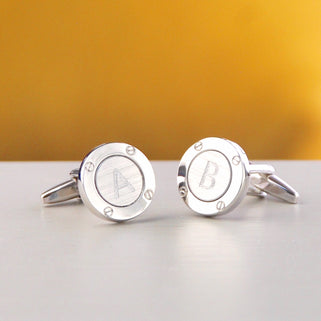Silver porthole cufflinks with initial "A" on the left cufflink and "B" on the right cufflink, shown in close up shot on yellow background.
