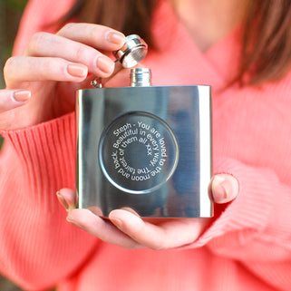 Silver hip flask with engraved spiral message on the front shown in close up shot with model.