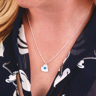 Sterling Silver Heart Charm and Blue Topaz/December birthstone charm on satellite chain necklace, shown in close up of model