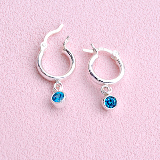 Sterling Silver Huggie Hoop Earrings with Blue Topaz/December birthstone charm, shown in close up shot