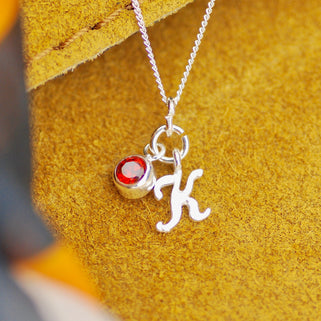 Sterling Silver Script Mini Initial "K"  Letter Necklace with July/Ruby Birthstone shown in close up shot on yellow background
