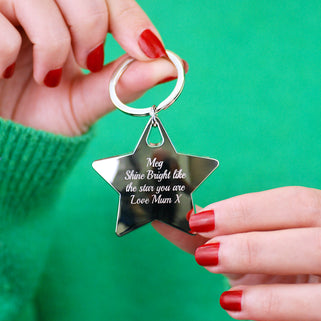 Christmas Star Keyring with Personalised message "Meg Shine Bright lie the star you are Love Mum X" engraved on the front shown in close up shot of model holding keyring with green background
