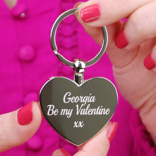 Silver heart keyring with personalised message "Georgia Be my Valentine xx" engraved on the front shown in close up with model.