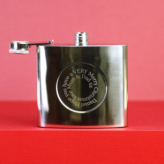 Silver hip flask with engraved spiral Christmas message on the front shown in close up shot on red background