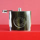 Silver hip flask with engraved spiral Christmas message on the front shown in close up shot on red background