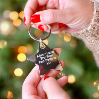 Christmas Star Keyring with Personalised message "Adam & Louise First Home First Christmas xxx" engraved on the front shown in close up shot of model holding keyring 